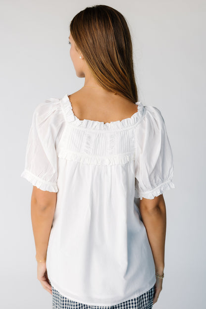 Back view of a woman wearing a white loose fitting blouse with a wide square neckline and back yoke pleat details