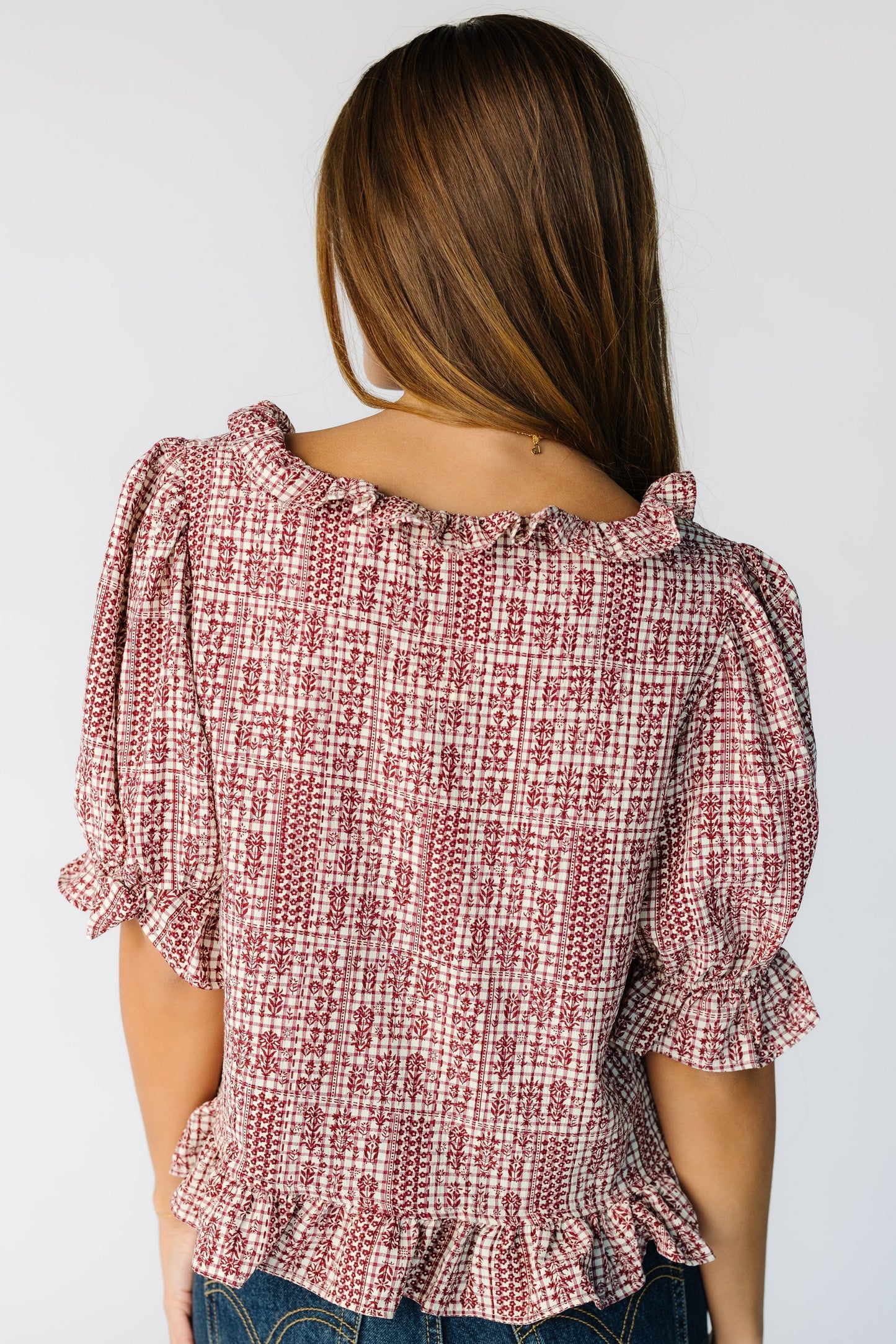 Back view of a woman wearing a loose fitting red plaid blouse with a ruffle neckline