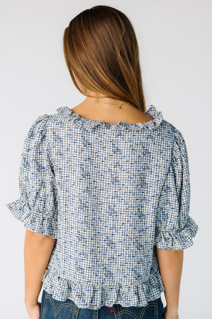 Back view of a woman wearing a loose  blue plaid top with a ruffle neckline with loose sleeves