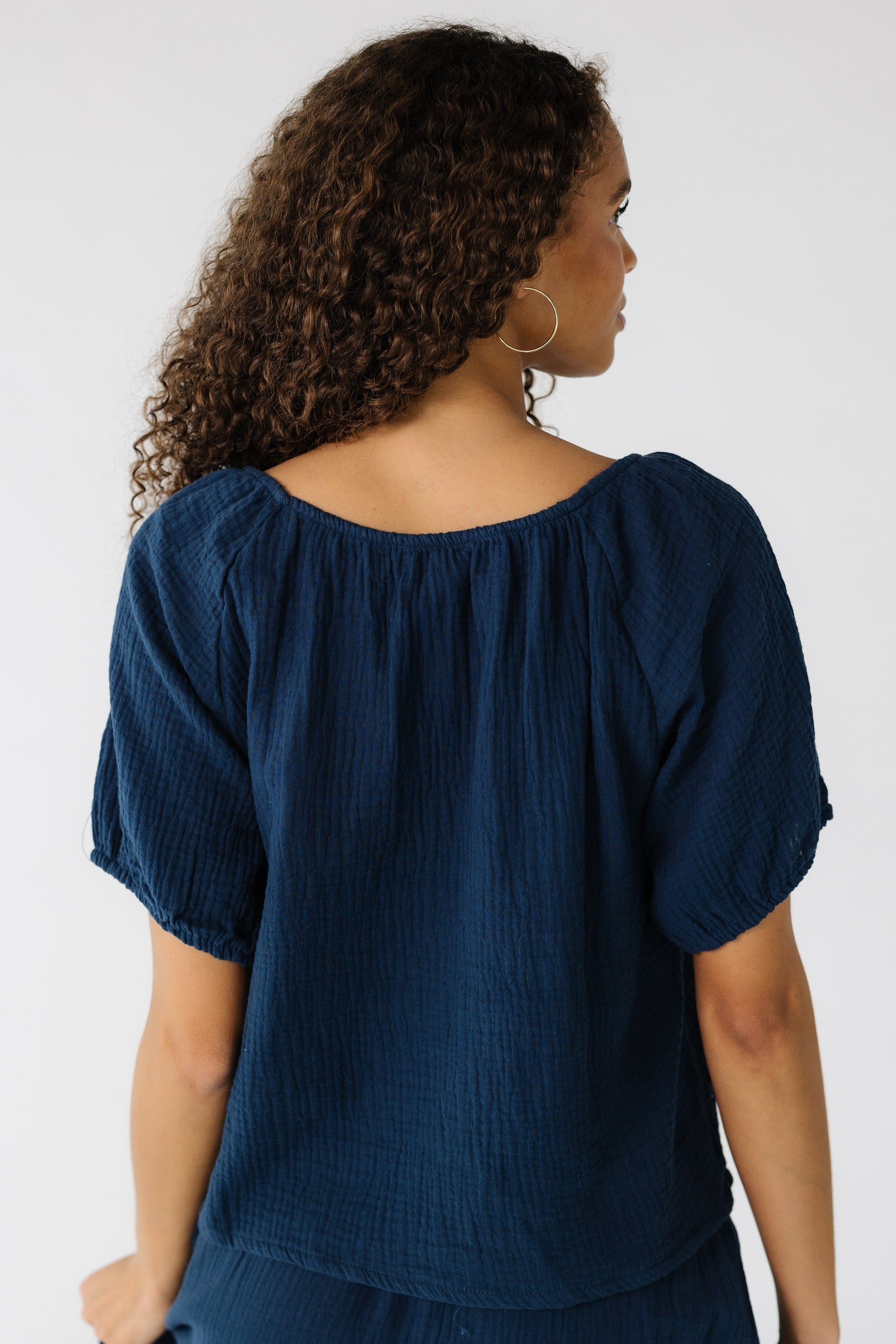 Back view of a teen girl wearing a loose fitting navy top with a round neckline and short sleeves.