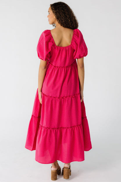 Back view of a teen girl wearing a pink gingham tiered dress with a square back neckline and large sleeves.