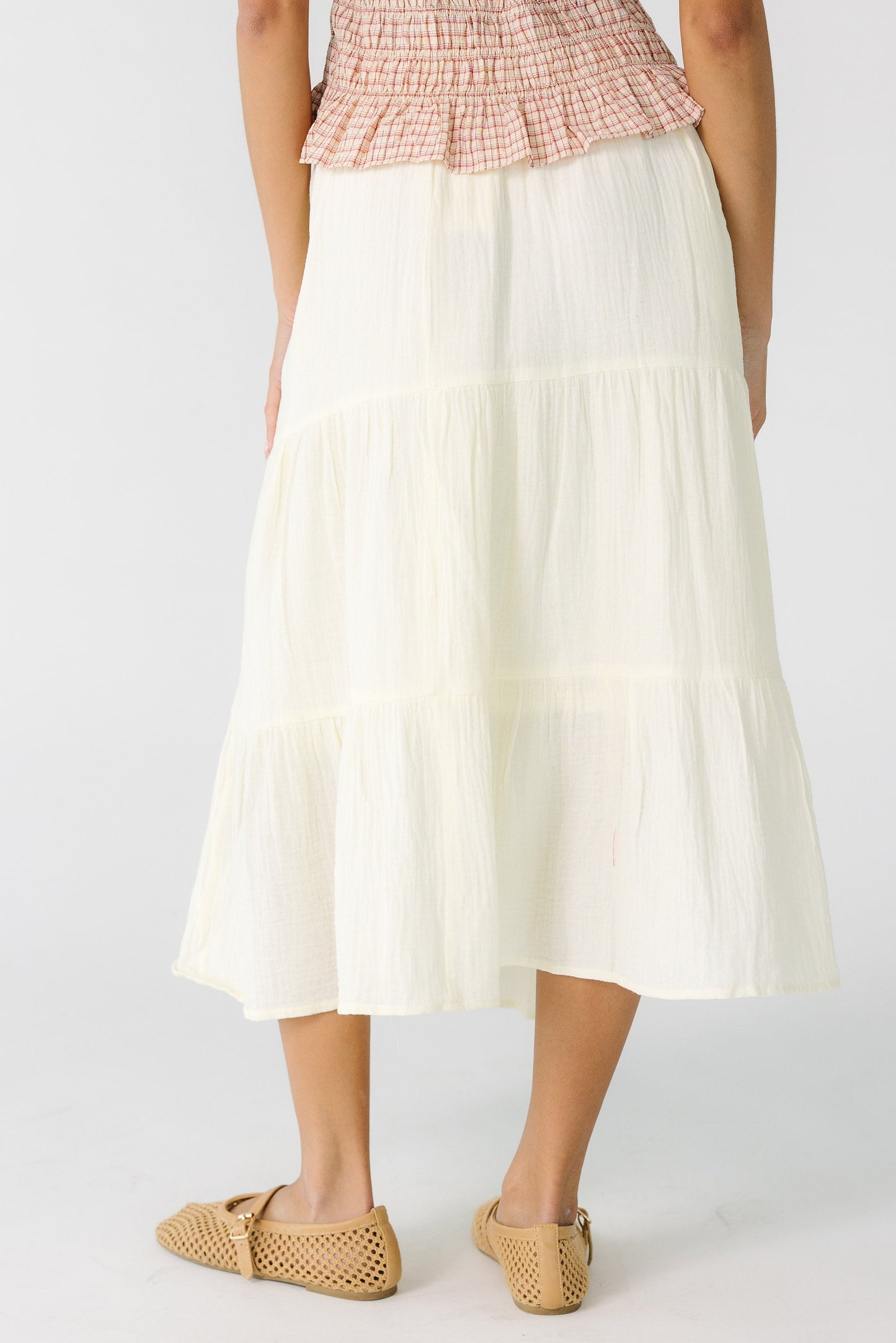 Back view of a teen girl wearing a cream tiered gauzy midi skirt.