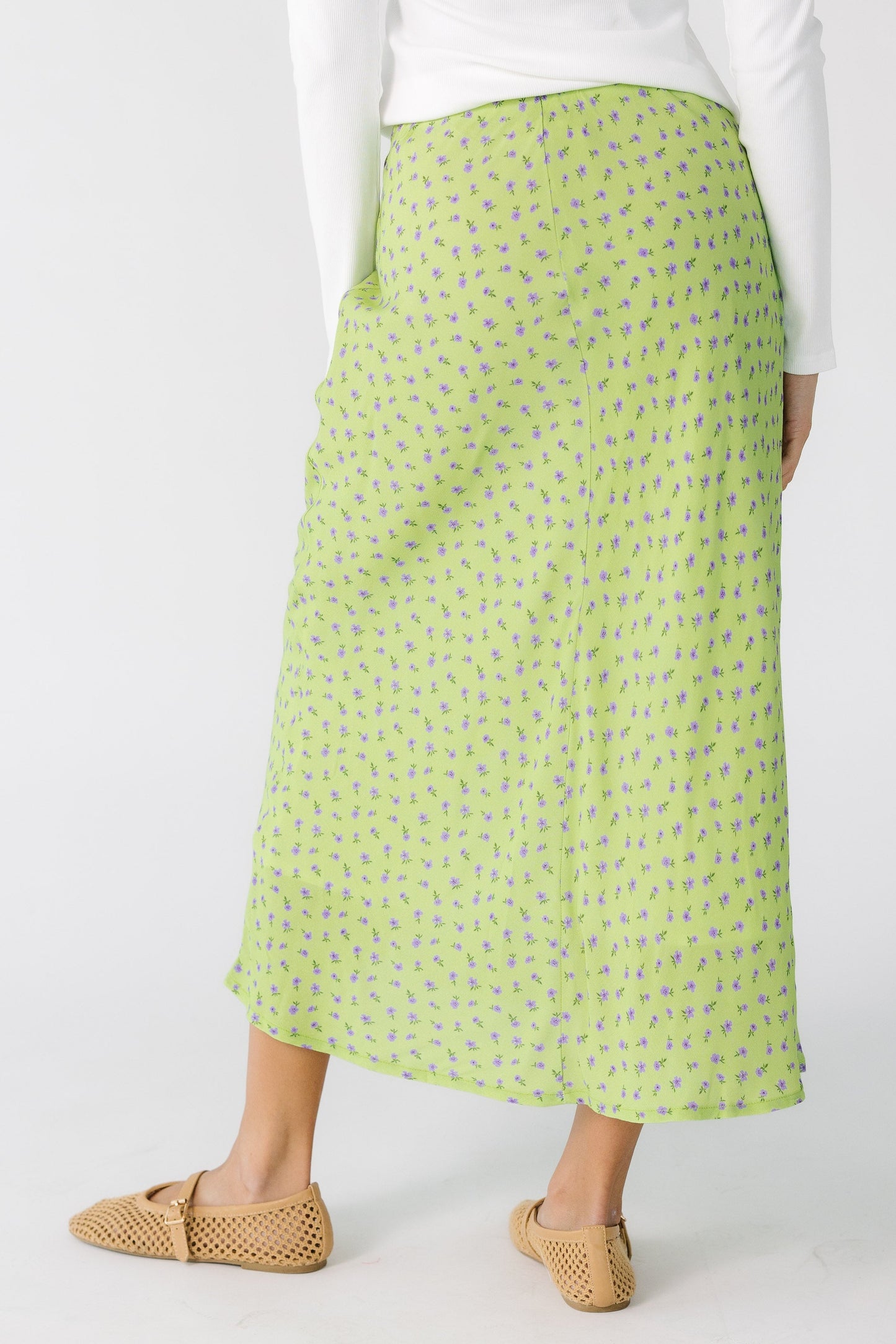 Back view of a teenage girl wearing a green floral print A-line skirt.