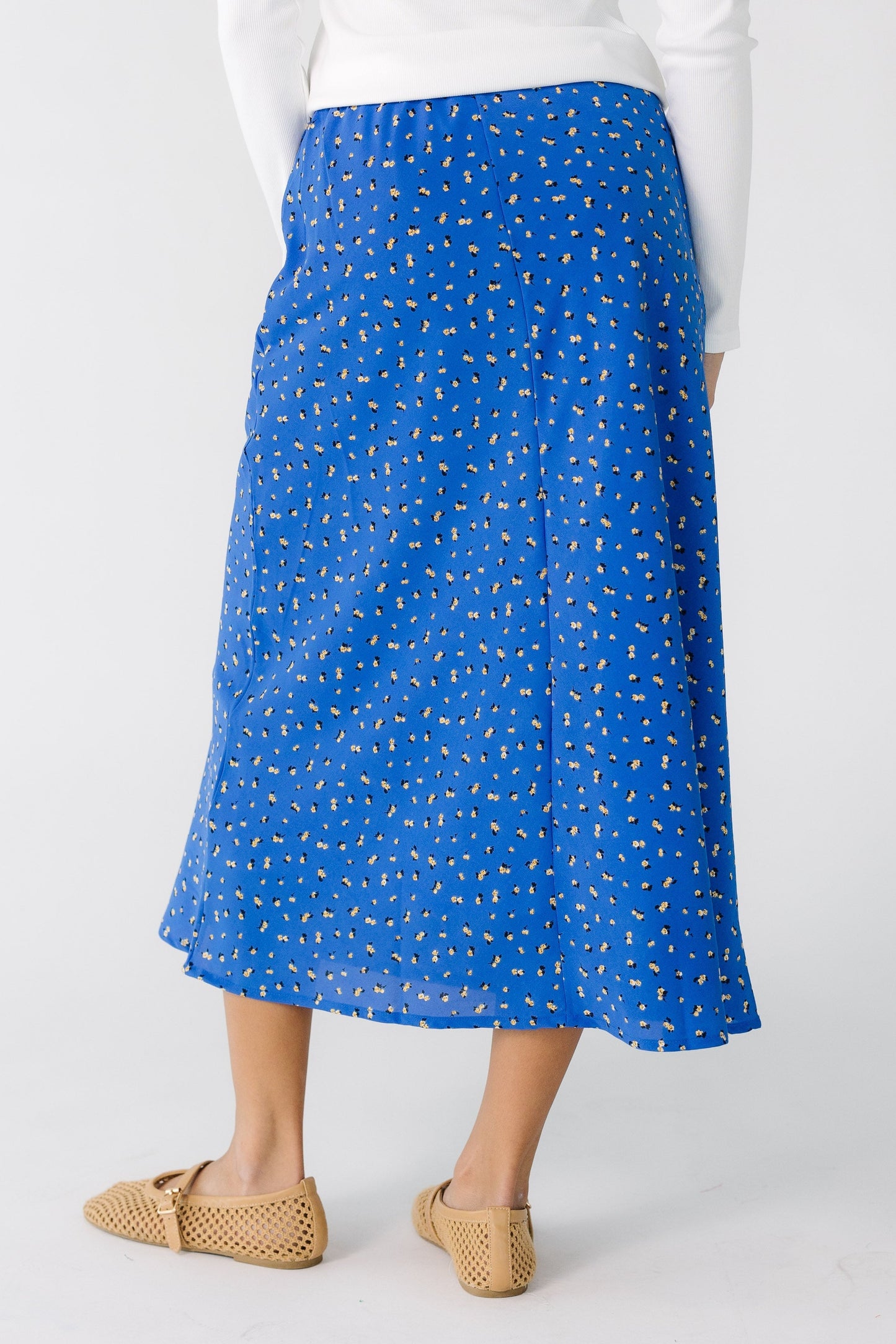 Back view of a teen girl wearing a blue floral A-line midi skirt.