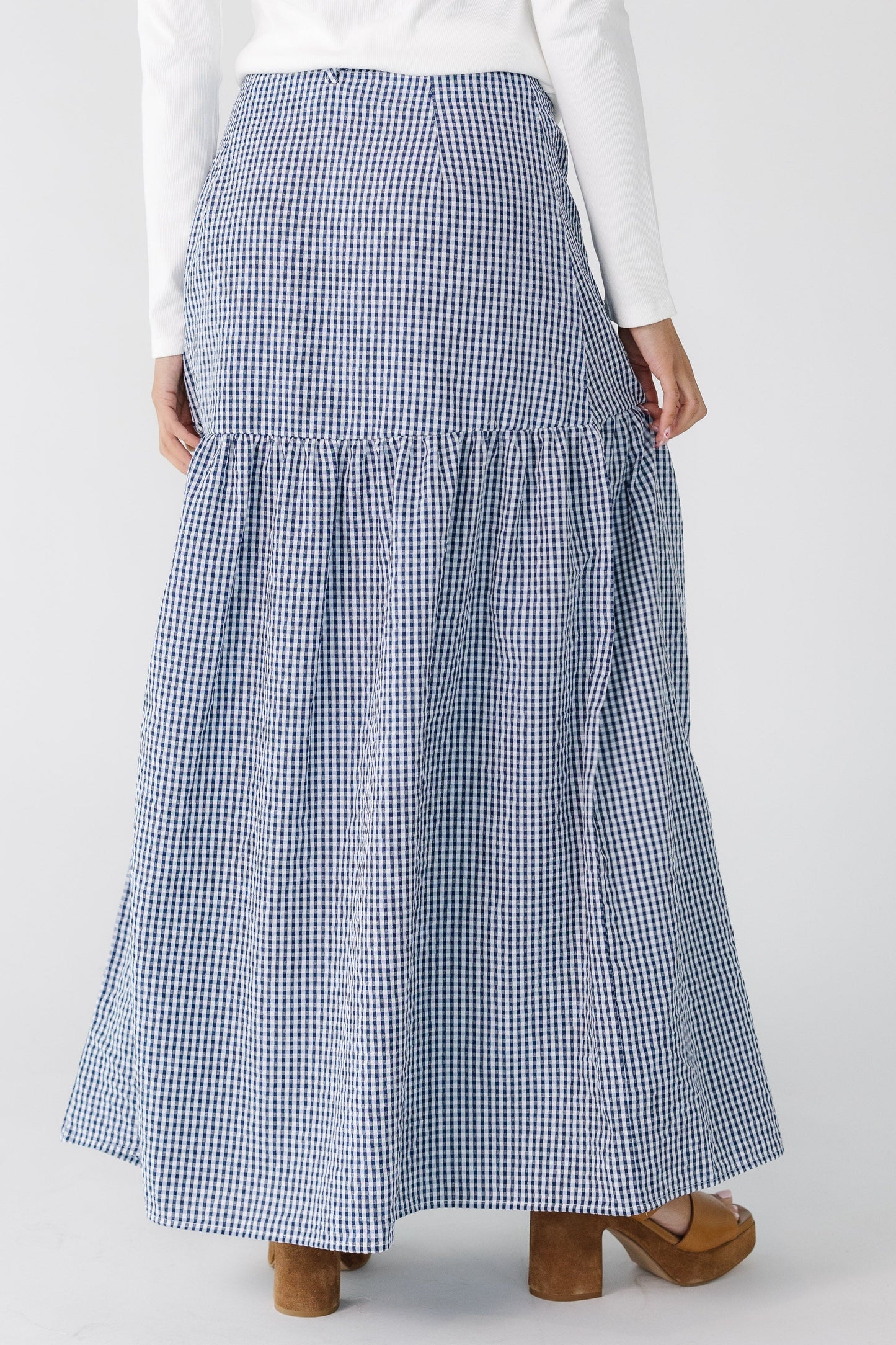 Back view of a teenage girl wearing a navy gingham, wrap  maxi skirt with a drop waist.