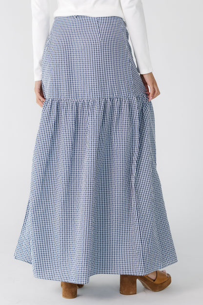 Back view of a teenage girl wearing a navy gingham, wrap  maxi skirt with a drop waist.