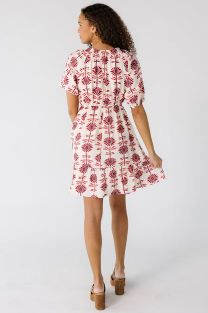Back view of a teen girl in a cream and mauve floral print dress with an elastic waist and short sleeves.