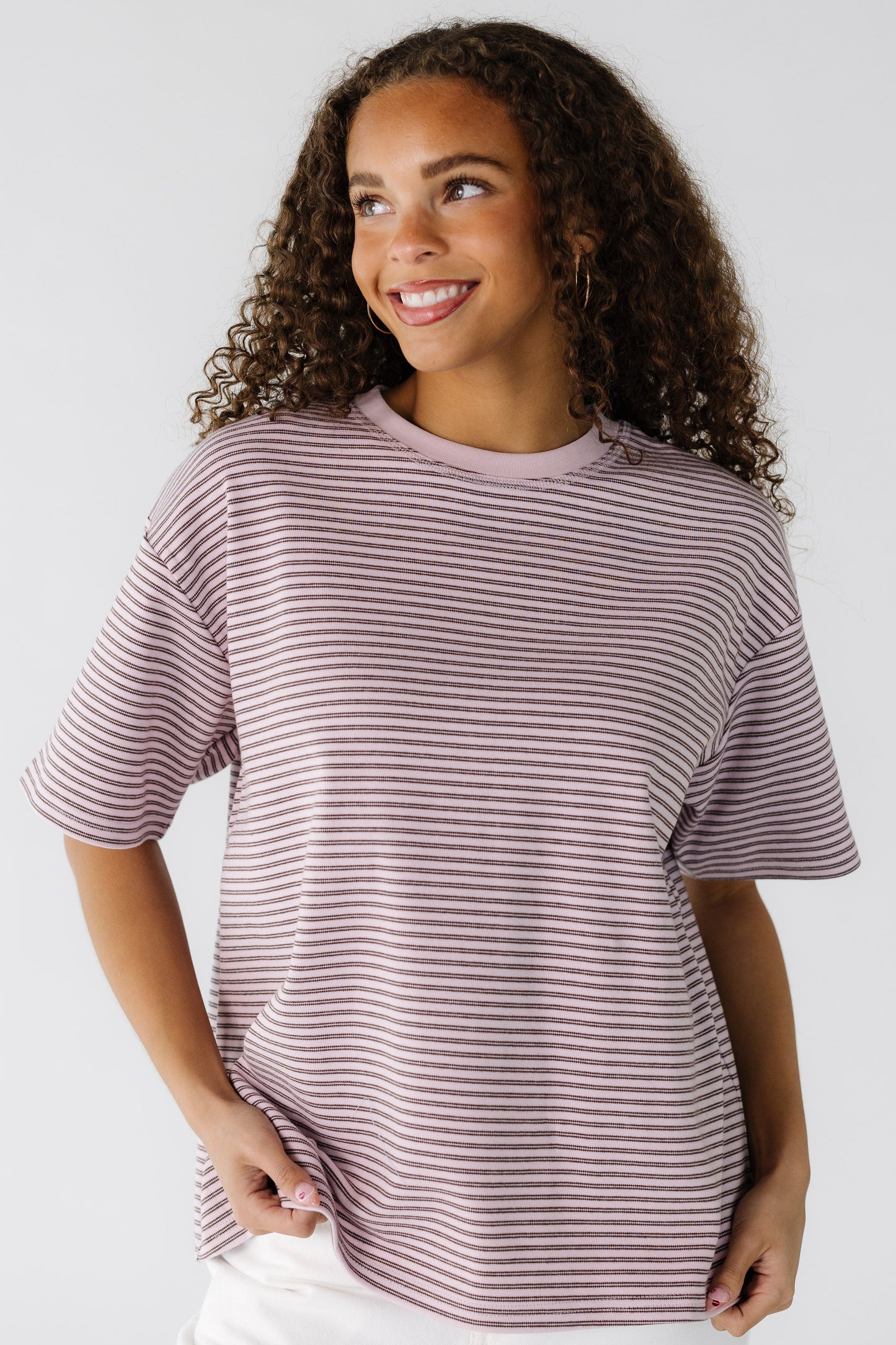 A teenage girl wearing a loose fitting pink and brown stripe tee.