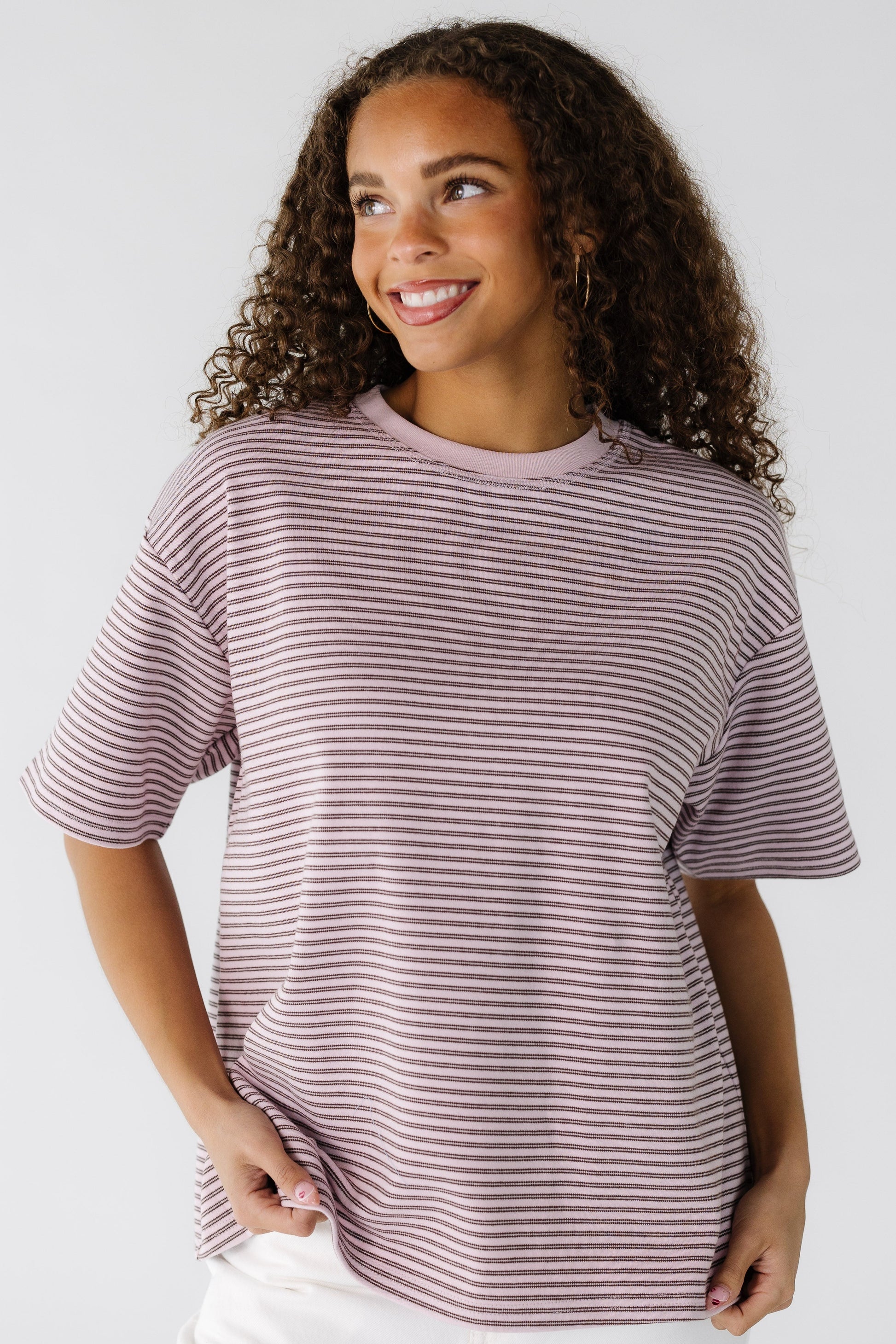 A teenage girl wearing a loose fitting pink and brown stripe tee.