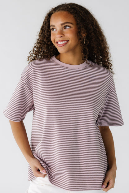 A teenage girl wearing a loose fitting pink and brown stripe tee.