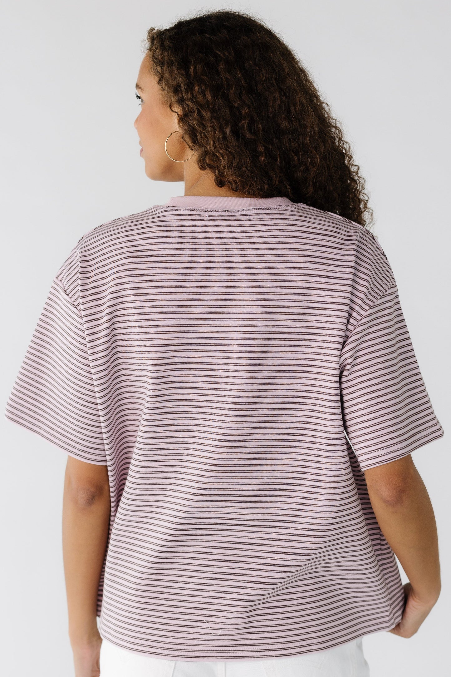 Back view of a young woman wearing a light pink tee with narrow double brown stripe with short sleeves.