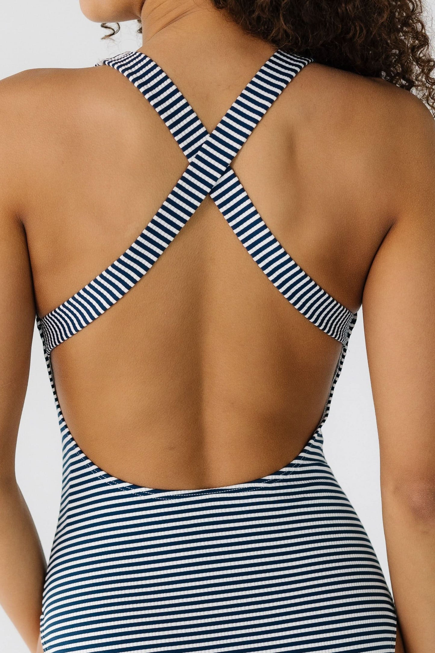 Close view of a young woman wearing a navy and white stripe one piece swimsuit with a scoop back neckline with wider crossed straps.