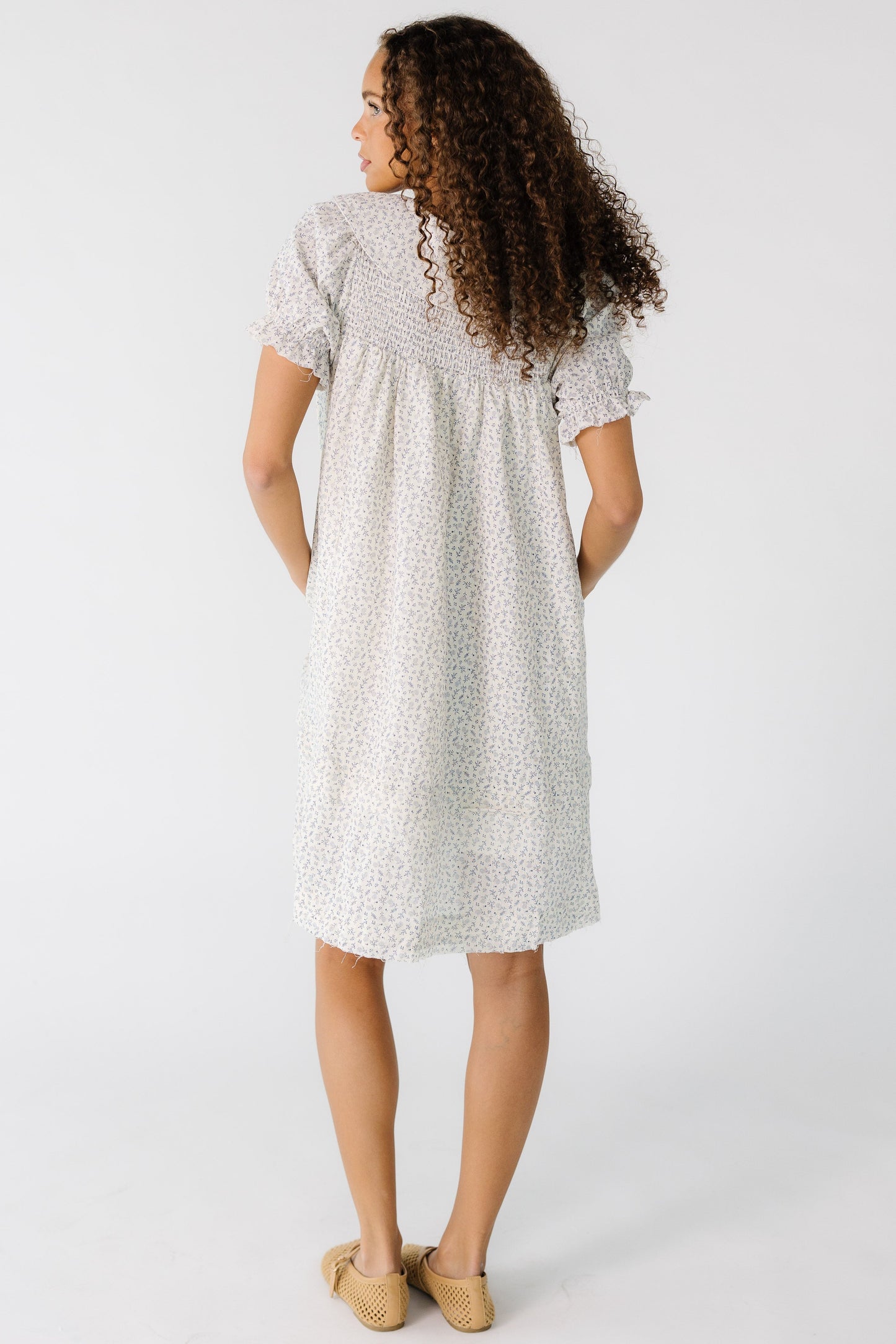 Back view of a  teen girl wearing a white and grey print dress that is cut above the knee with a smocked back yoke and short sleeves.