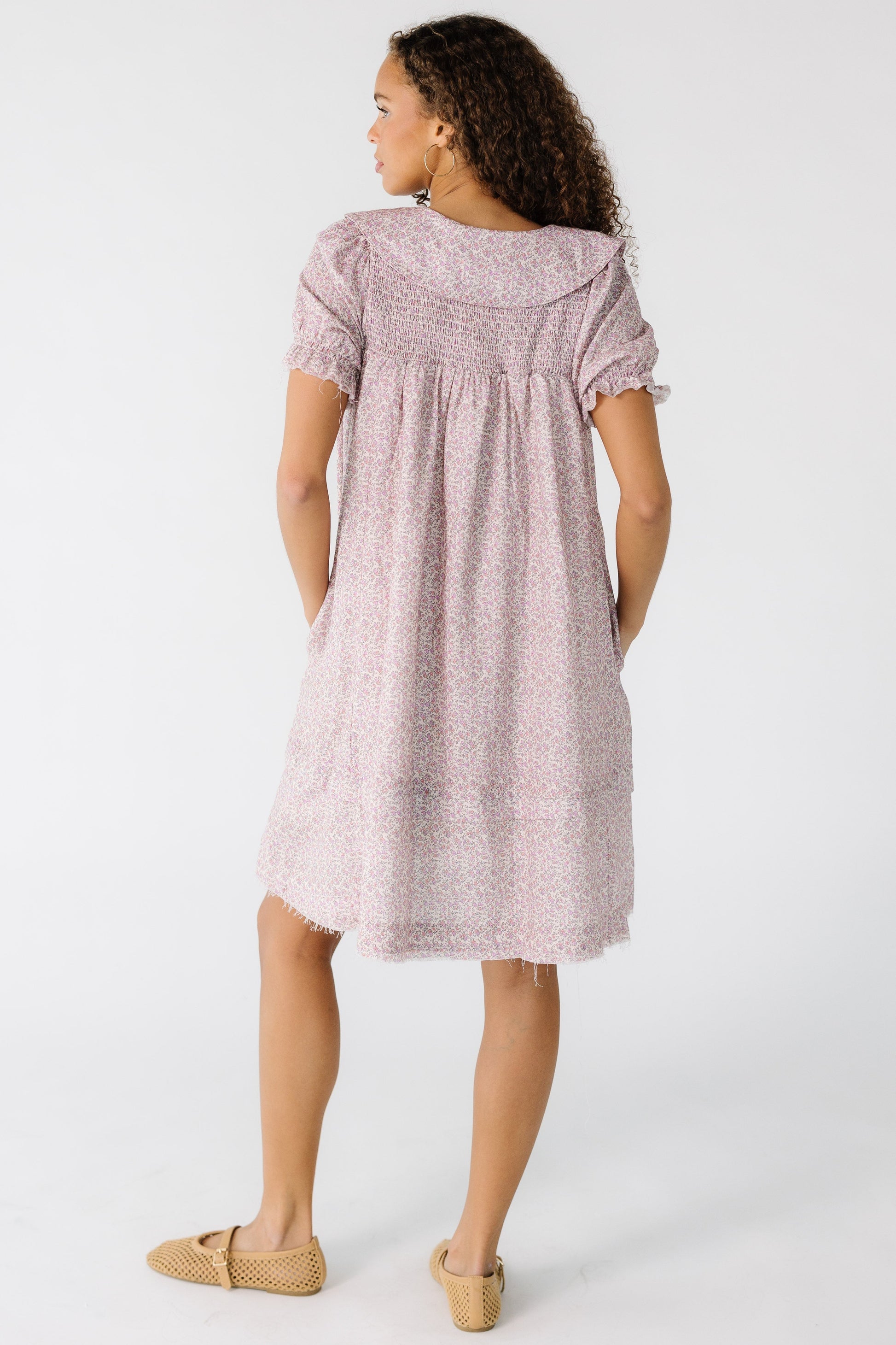 Back view of a teen girl wearing a pink floral short dress with short sleeves and a smocked back yoke.
