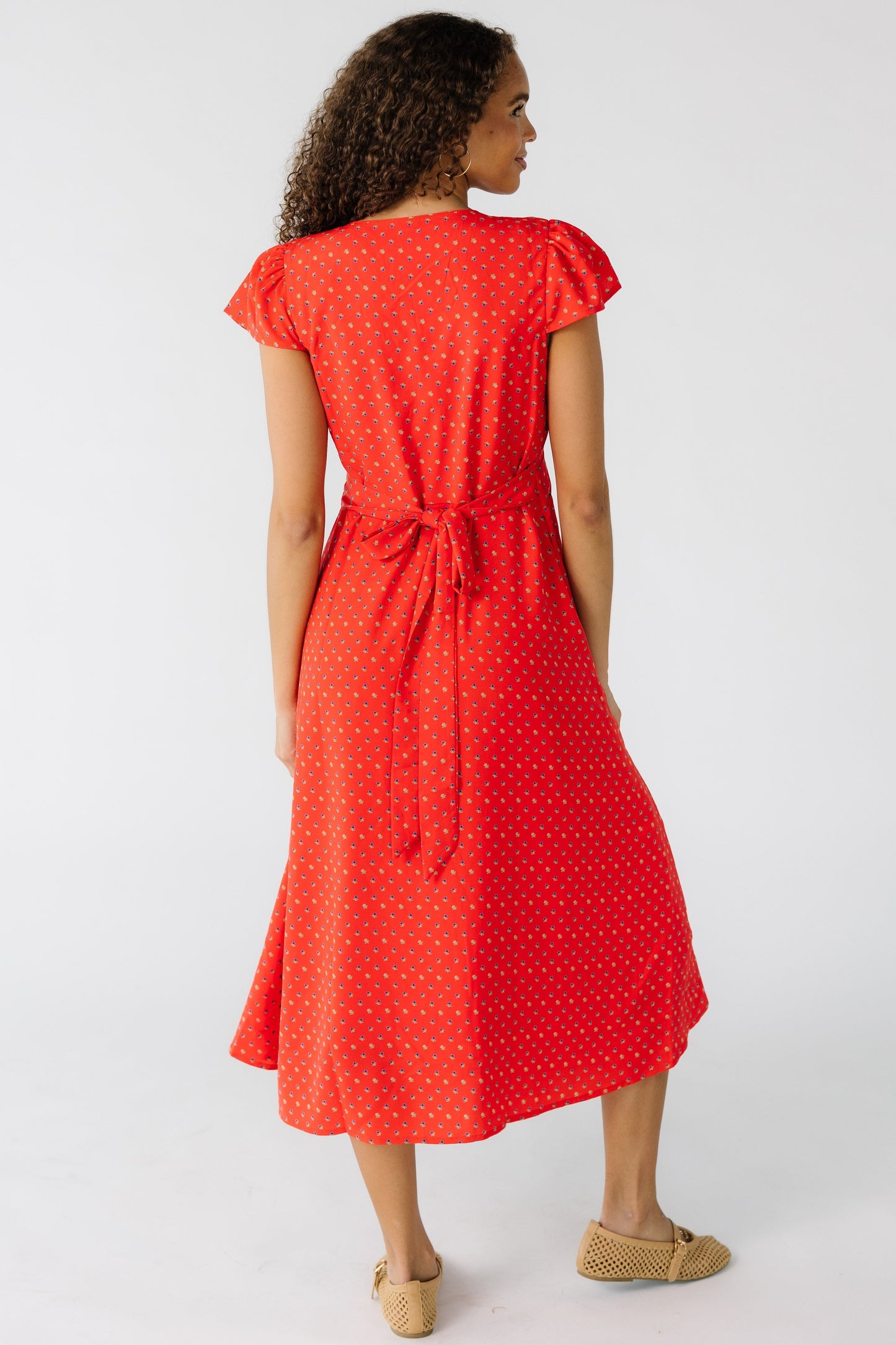 Back view of a teen girl wearing a red floral midi dress with short flutter sleeves and a back tie.