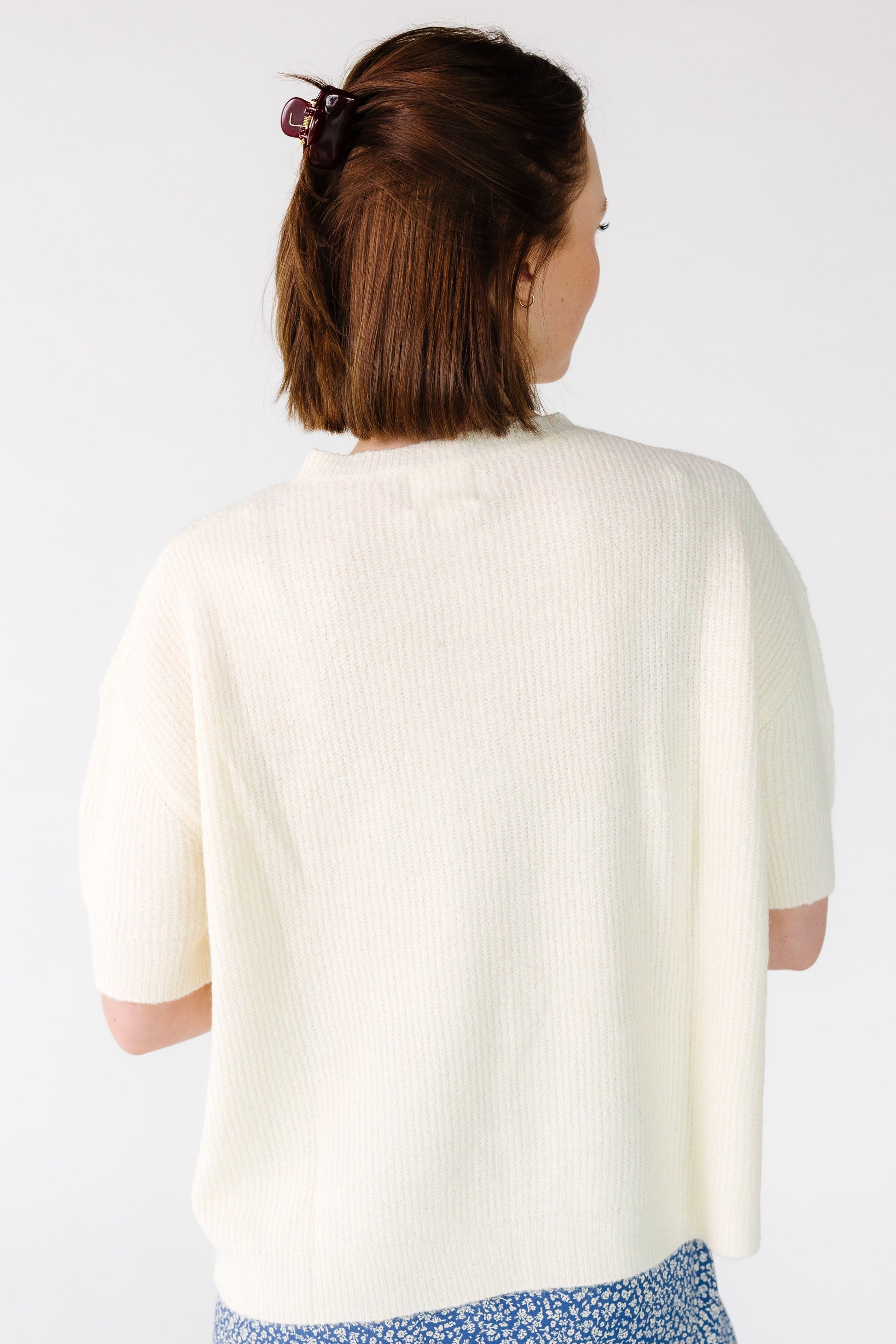 Back view of a young woman wearing an ivory loose fitting cardigan with short sleeves.