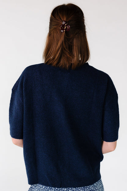 Back view of a young woman wearing a navy rib knit, loose fitting cardigan with short sleeves.