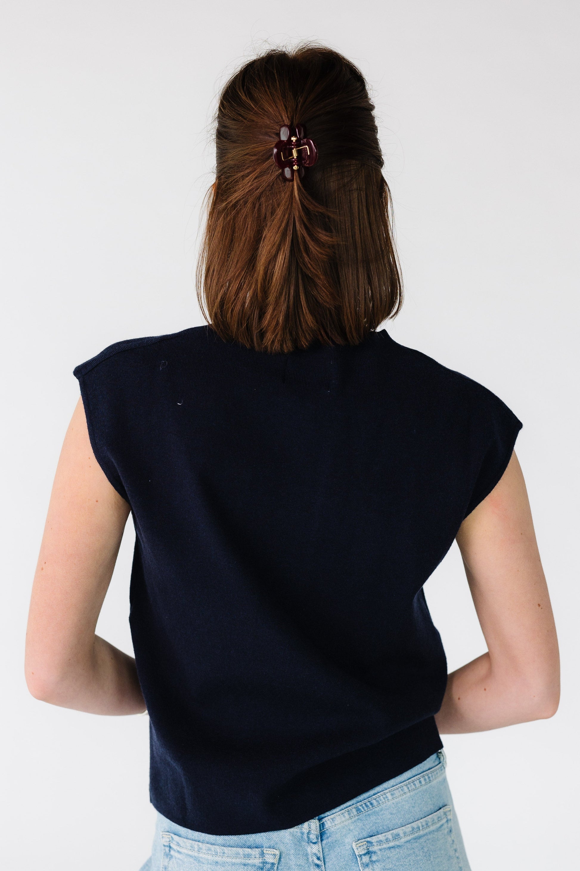 Back view of a young woman wearing a navy sleeveless, loose fitting sweater vest.