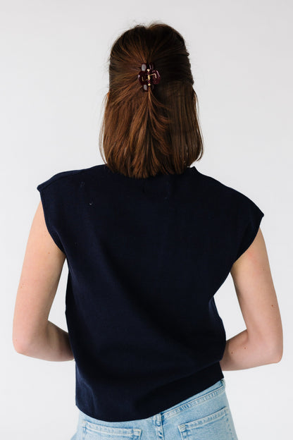 Back view of a young woman wearing a navy sleeveless, loose fitting sweater vest.