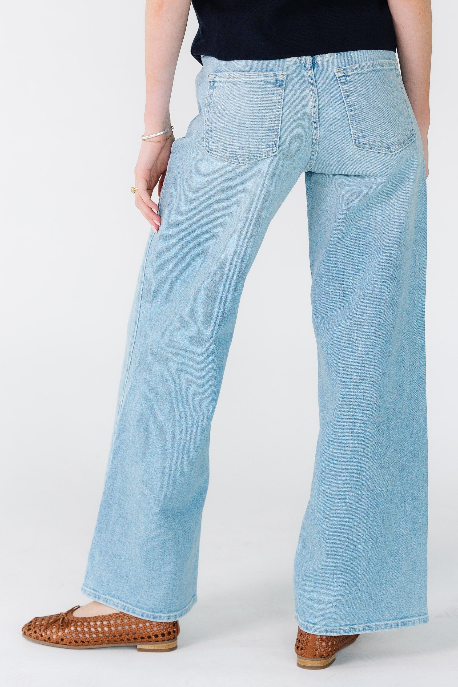 Back view of a woman wearing a pair of wide leg denim jeans with back pockets and sewn hem.