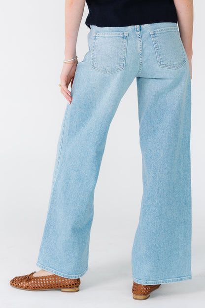 Back view of a woman wearing a pair of wide leg denim jeans with back pockets and sewn hem.