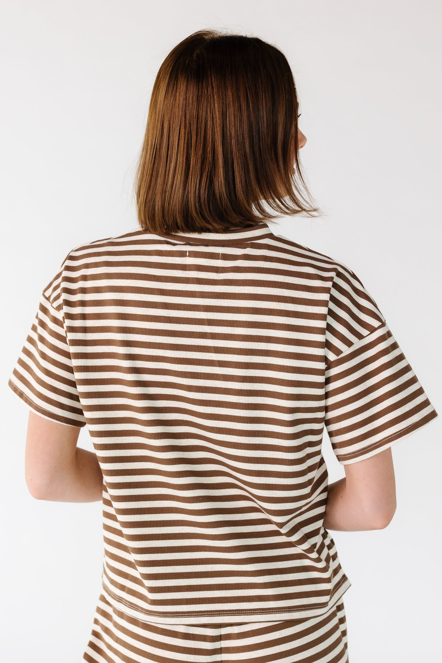 Back view of a young woman wearing a brown and cream stripe tee with short sleeves.