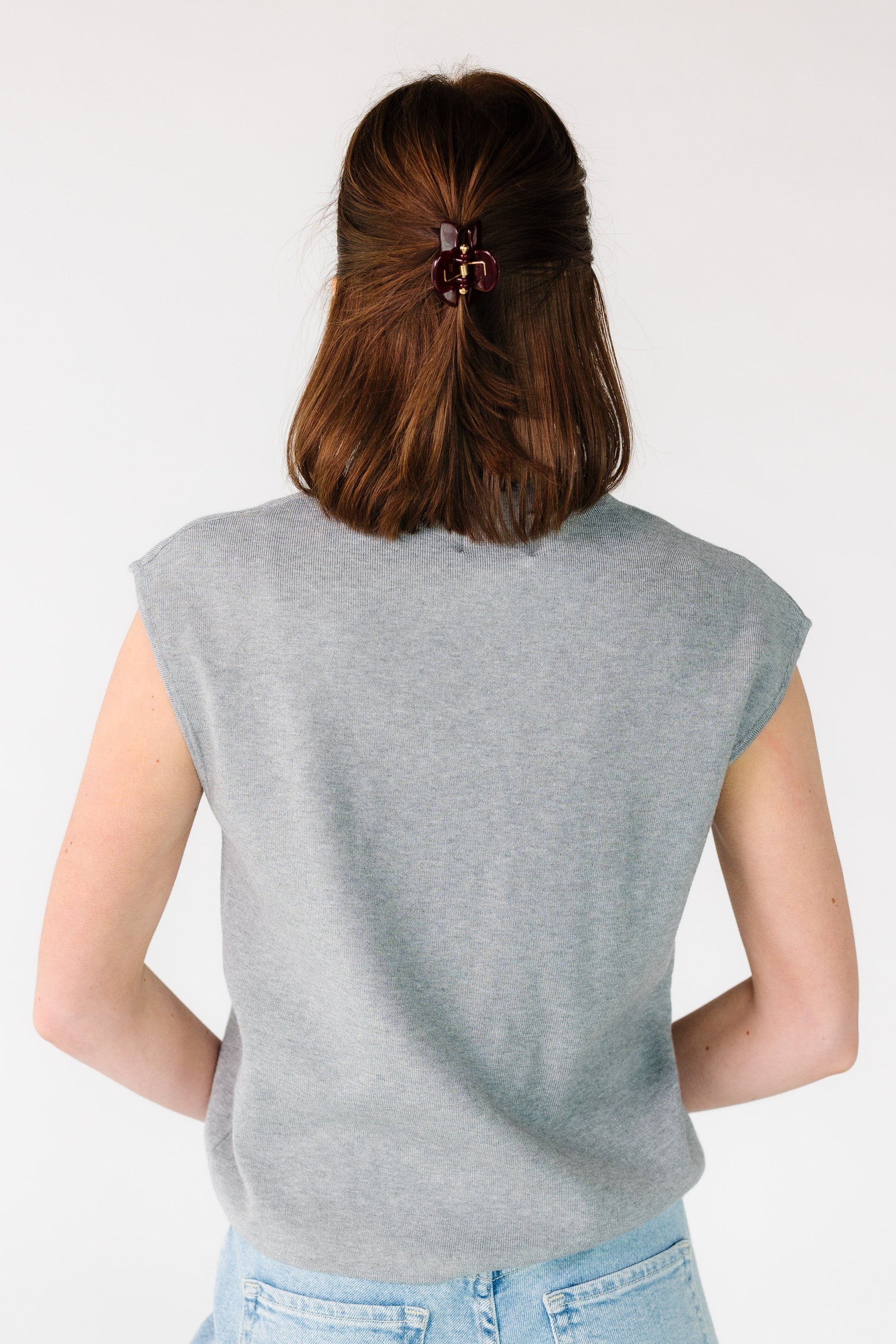 Back view of a woman wearing a grey loose loose fitting sweater vest.