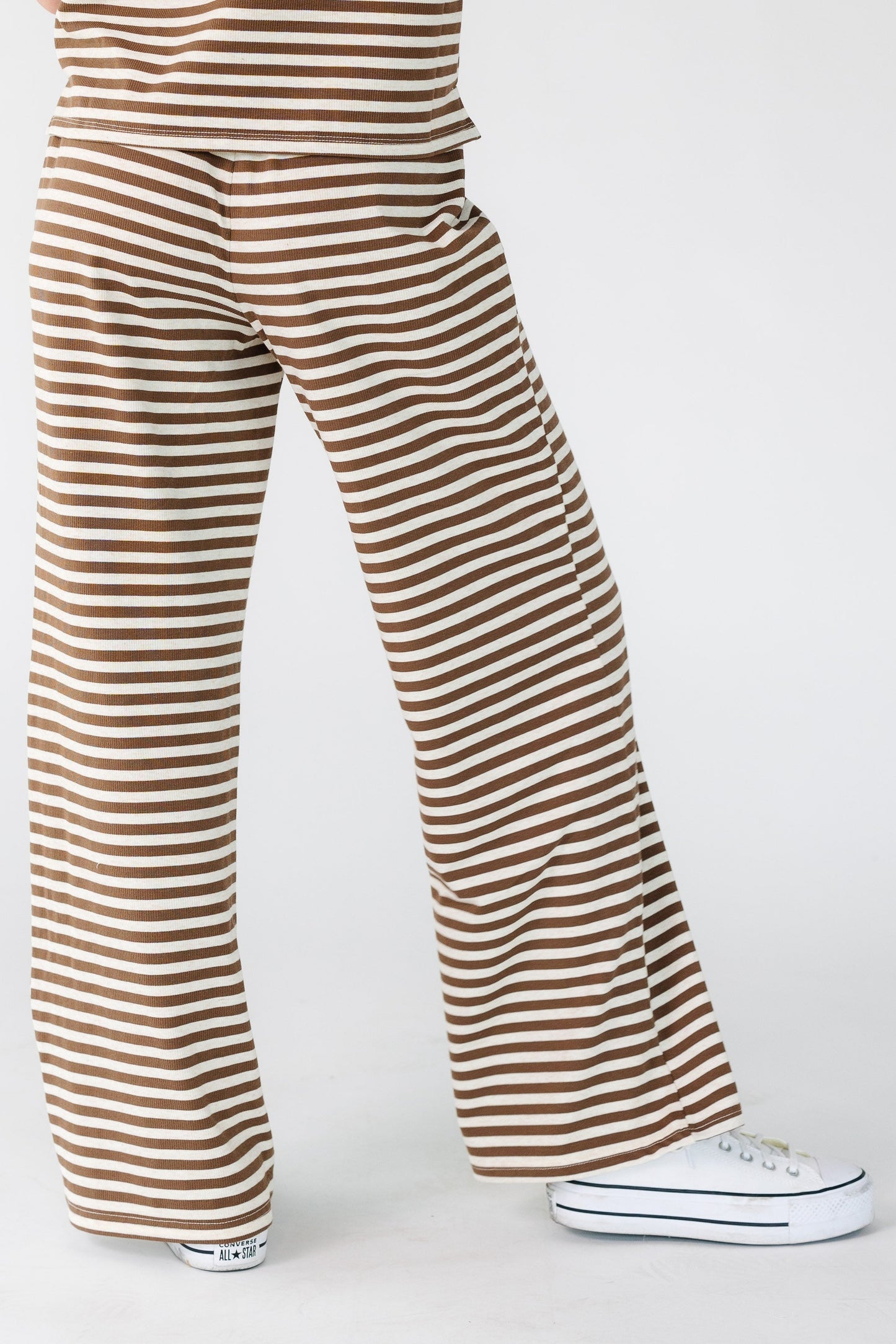 Back view of a woman wearing a pair of wide leg lounge pants in brown and cream stripe.