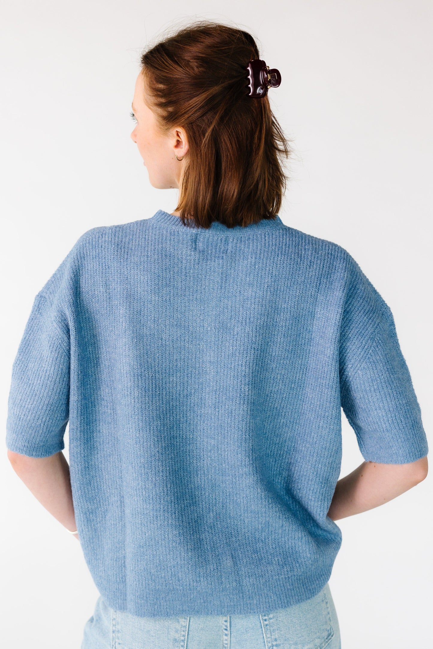 Back view of a woman wearing a dusty blue cardigan that is loose fitting and has short sleeves.