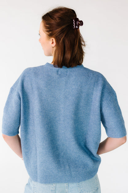 Back view of a woman wearing a dusty blue cardigan that is loose fitting and has short sleeves.
