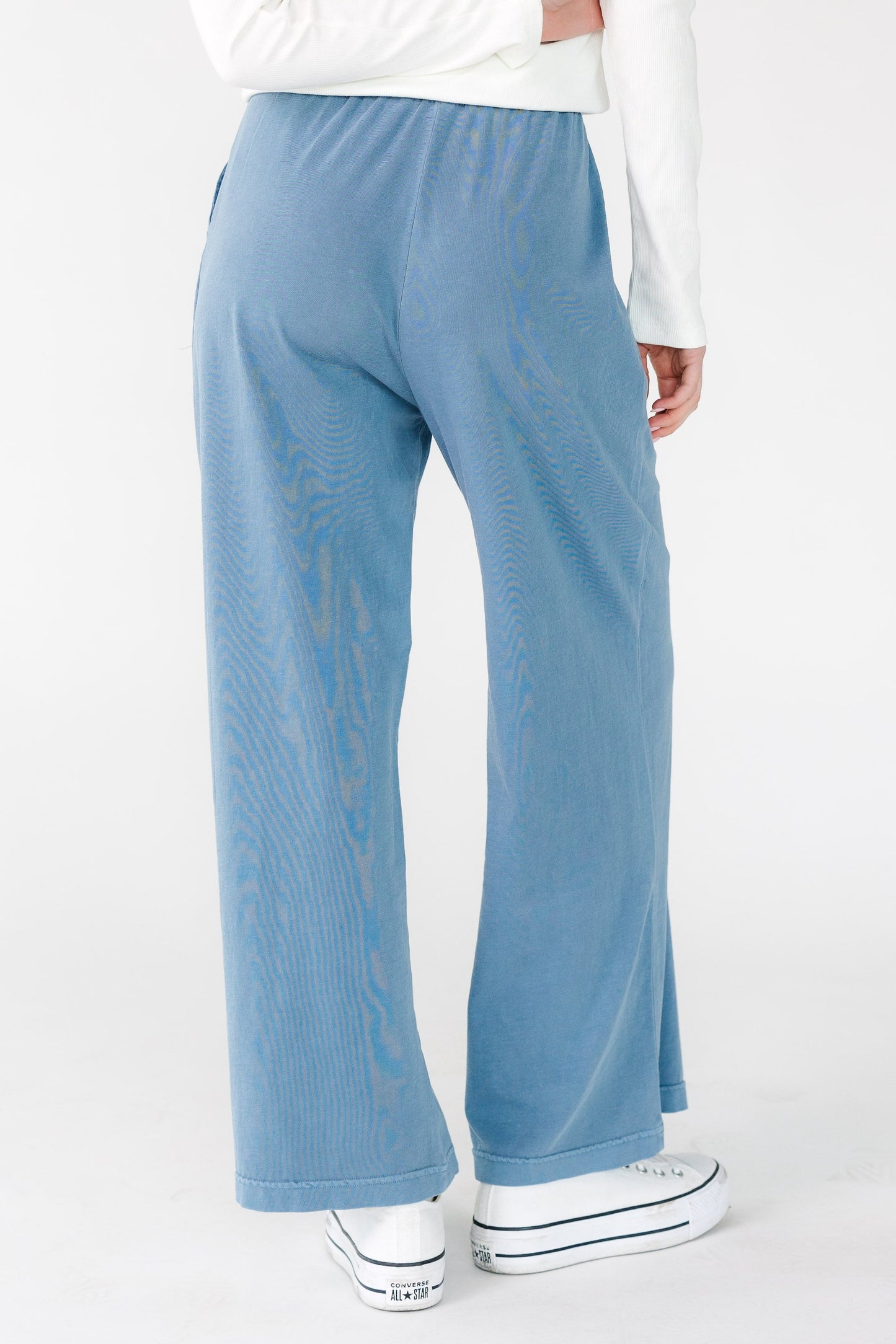 Back view of a young woman wearing a pair of wide leg blue pants.