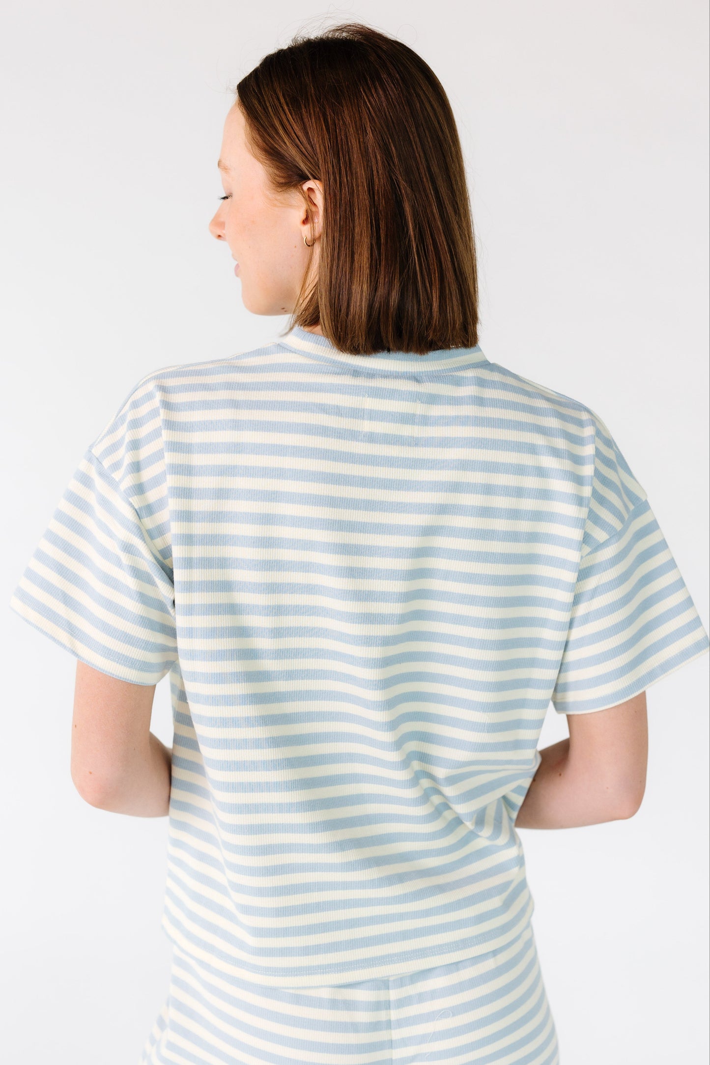 Back view of a woman wearing a light blue and white stripe ribbed top with short sleeves.