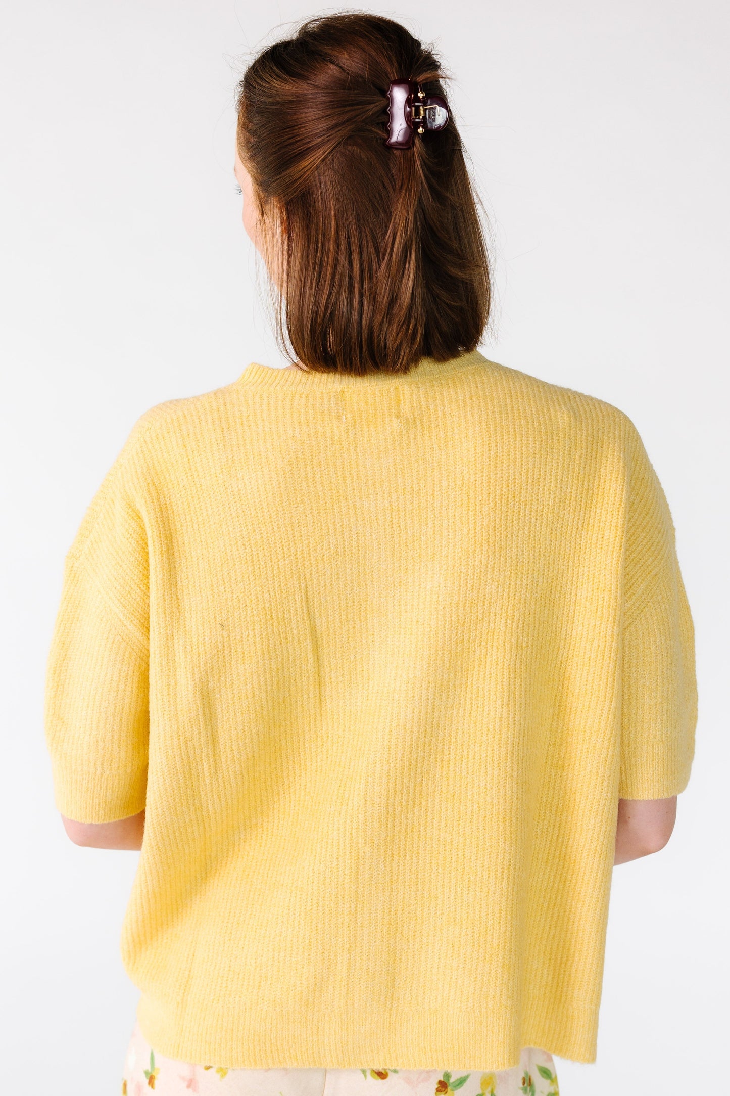 Back view of a young woman wearing a yellow ribbed cardigan with short sleeves.