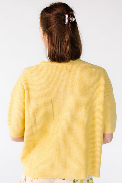 Back view of a young woman wearing a yellow ribbed cardigan with short sleeves.