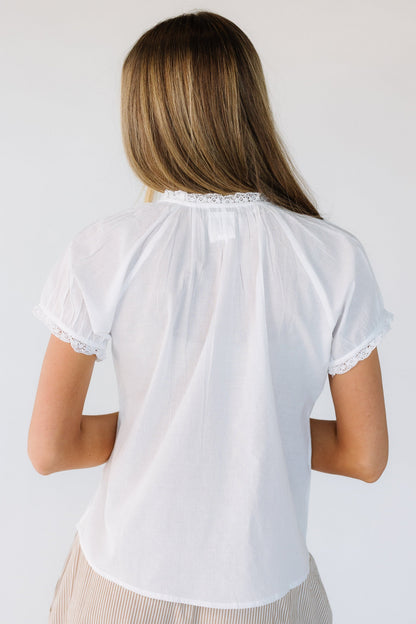 Back view of a woman wearing a white blouse with short, lace hemmed sleeves and a high round neckline with lace trim.