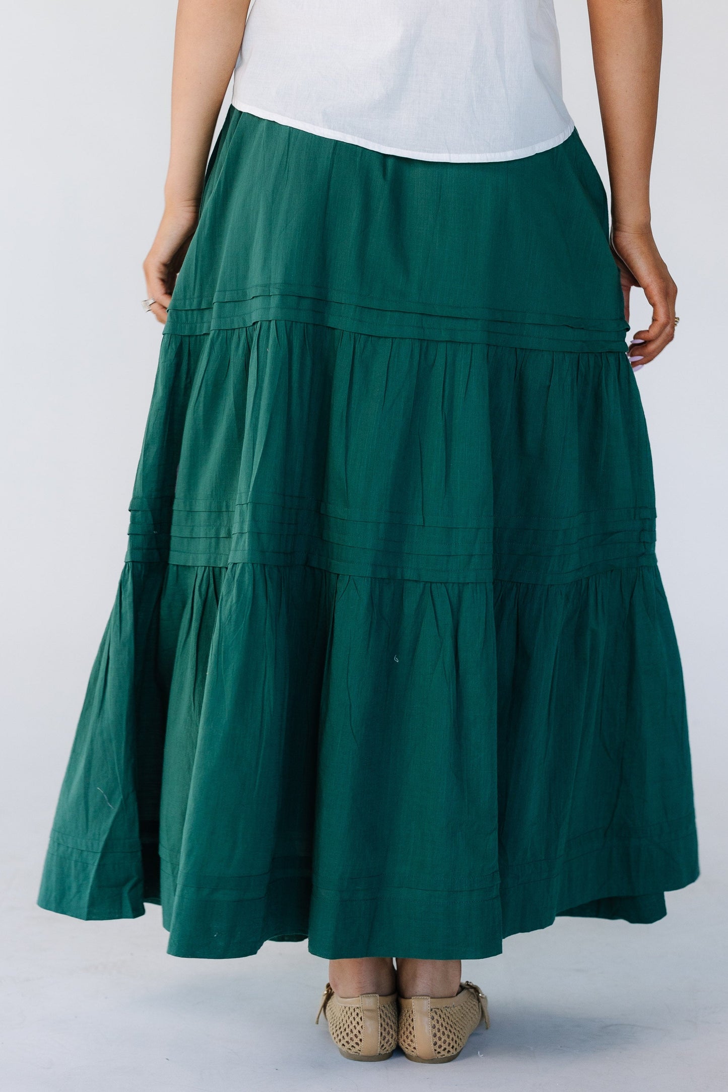Back view of a woman wearing a green tiered midi skirt with horizontal pleats.
