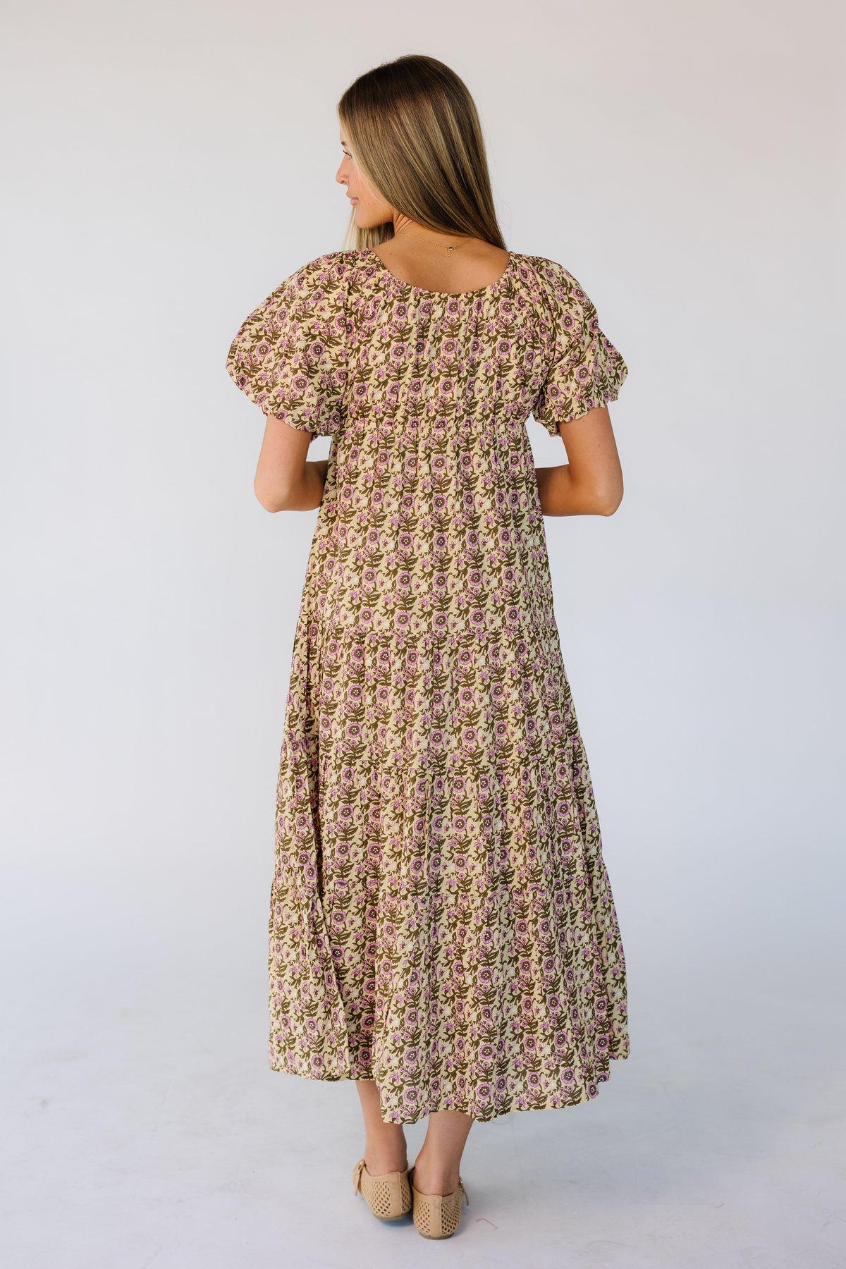 Back view of a woman wearing a green & pink floral print midi dress with large puff sleeves.