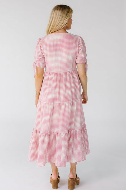 Back view of a woman wearing a pink and white gingham midi dress with a gathered waist and short sleeves.