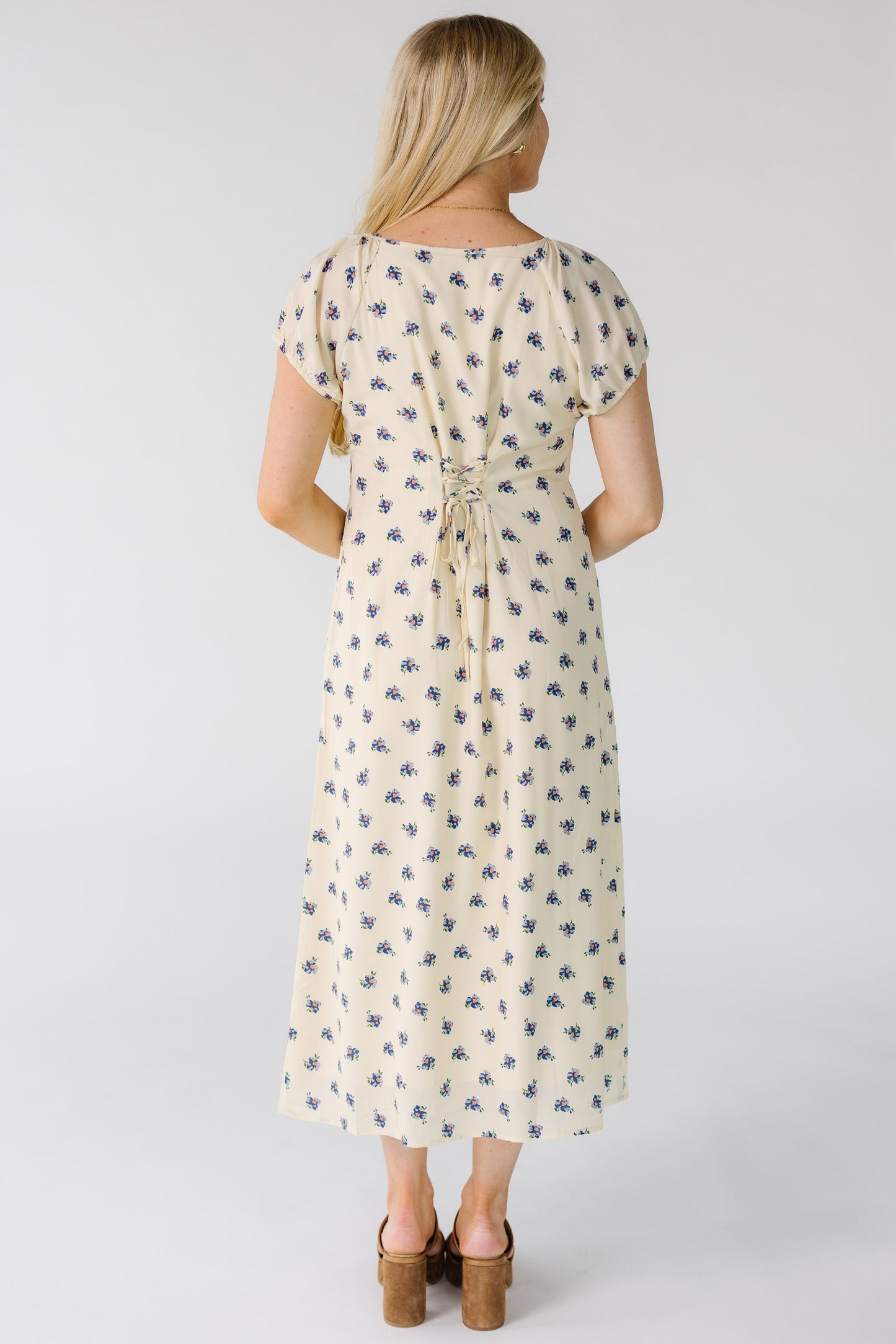 Back view of a woman wearing a cream midi dress with blue floral print and back lacing details.