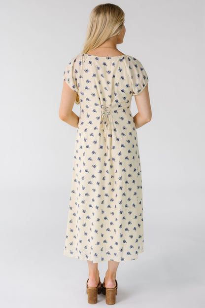 Back view of a woman wearing a cream midi dress with blue floral print and back lacing details.