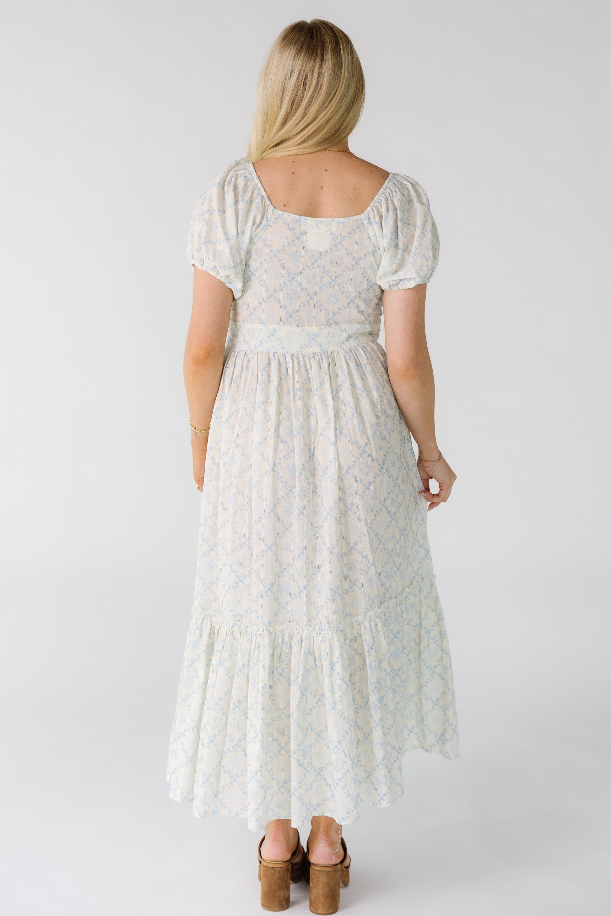 Back view of a woman wearing a white floral midi dress with square back neckline with short puff sleeves.