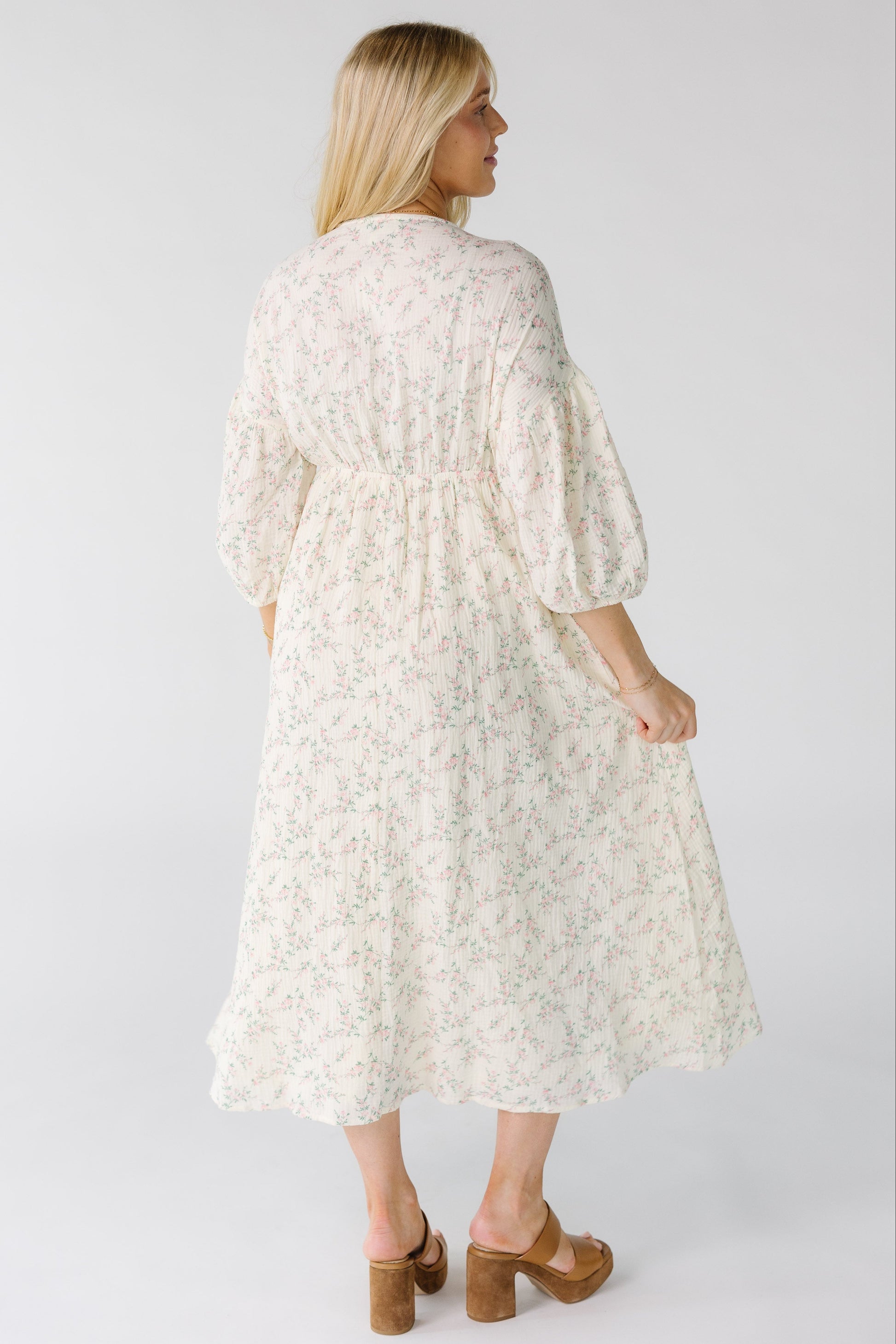 Back view of a woman wearing an ivory floral print midi dress with pink floral print with a back elastic waistband.