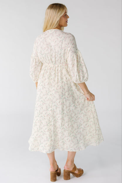 Back view of a woman wearing an ivory floral print midi dress with pink floral print with a back elastic waistband.