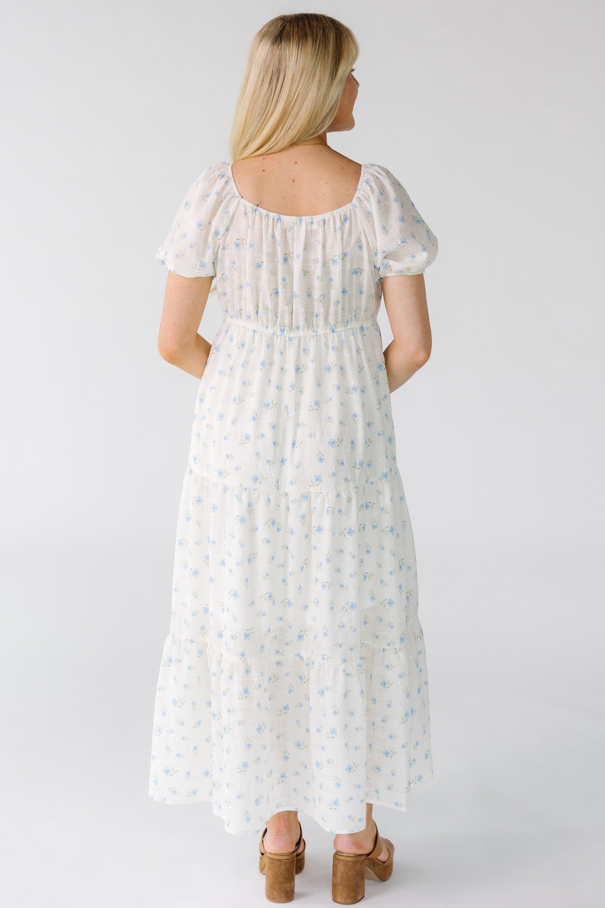 Back view of a woman wearing a white floral print midi dress with a square back neckline and short puff sleeves.