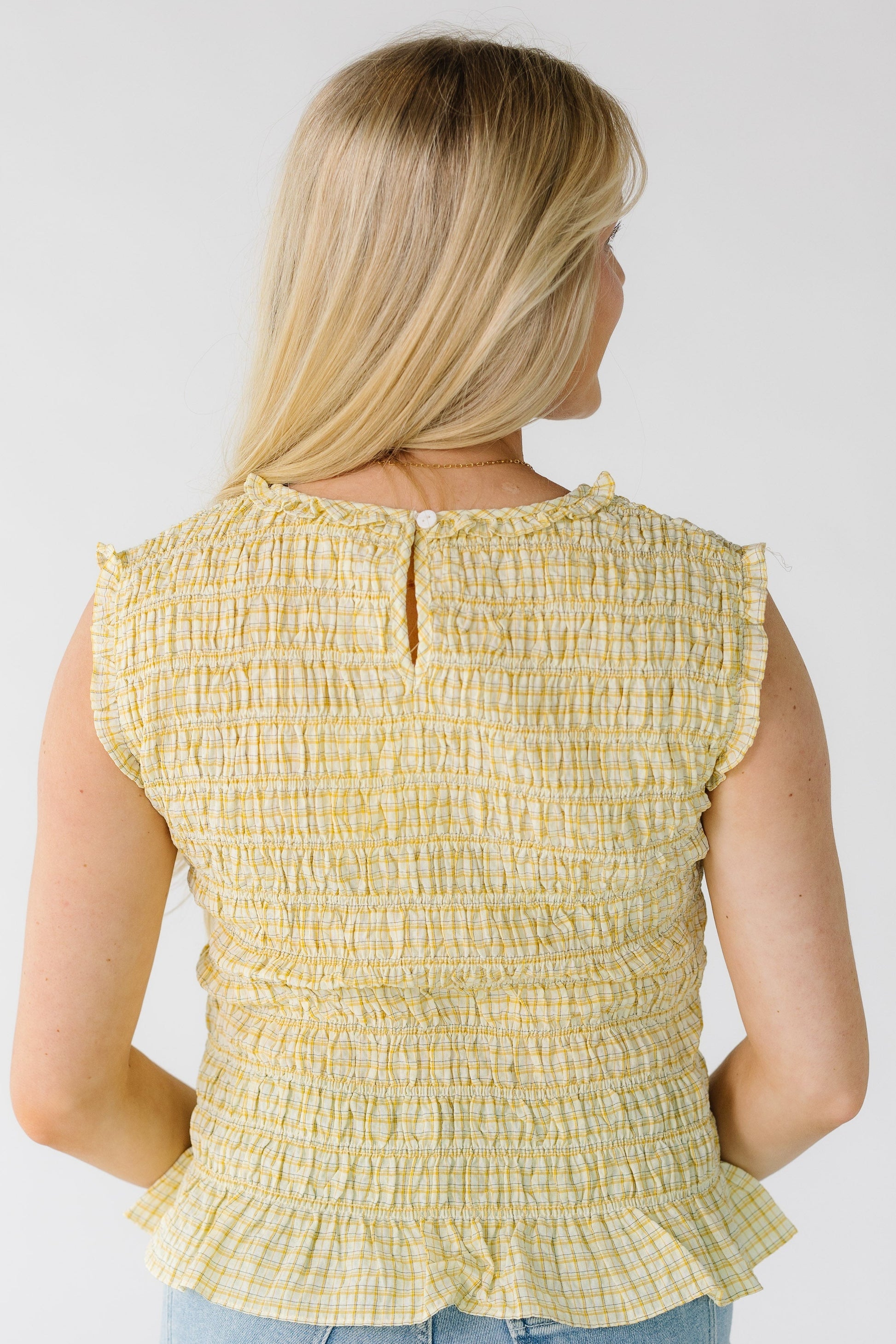 Back view of a woman wearing a yellow smocked bodice to[ with a button-keyhole closure.