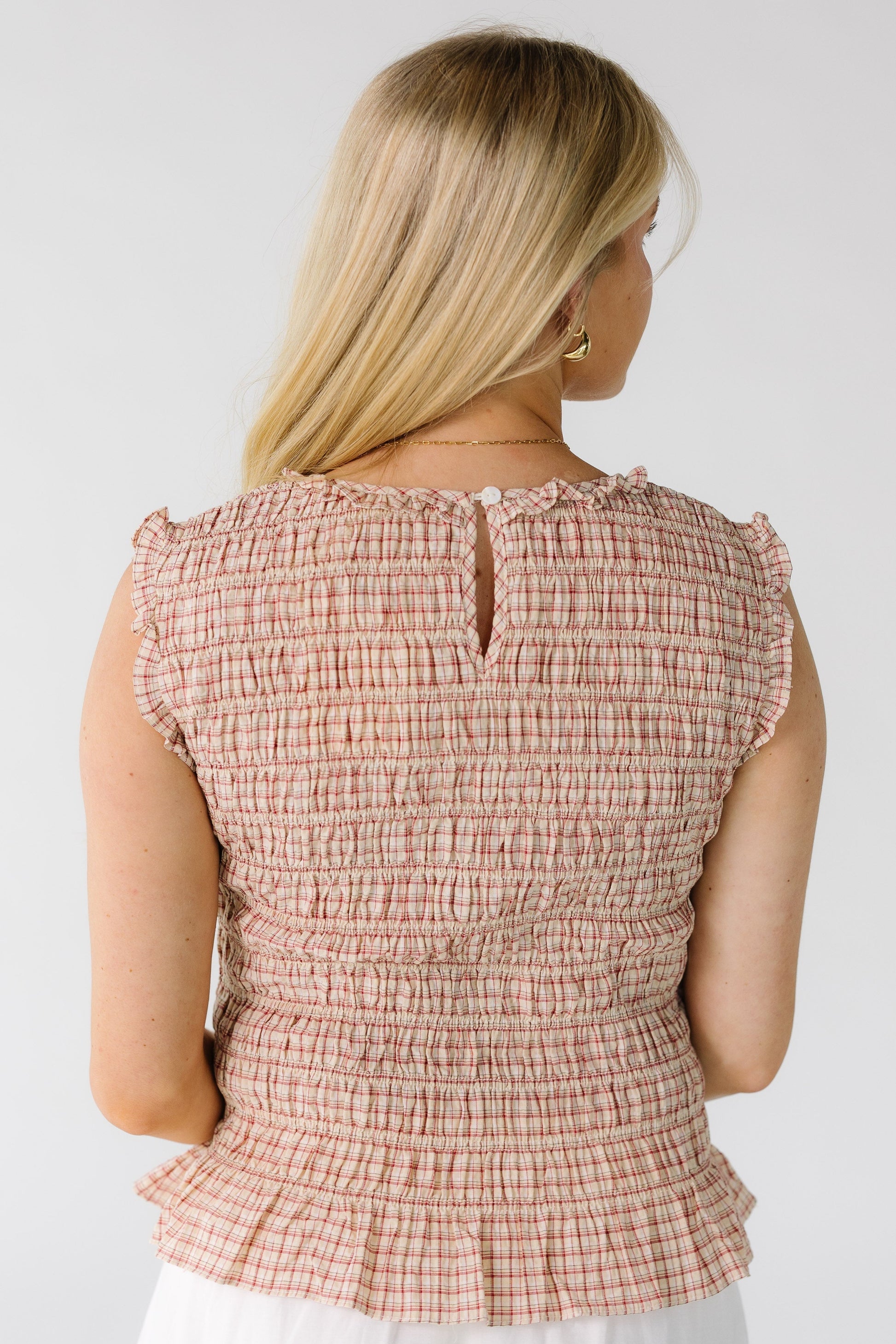 Back view of a woman wearing a red plaid smocked bodice top with a button-keyhole closure.