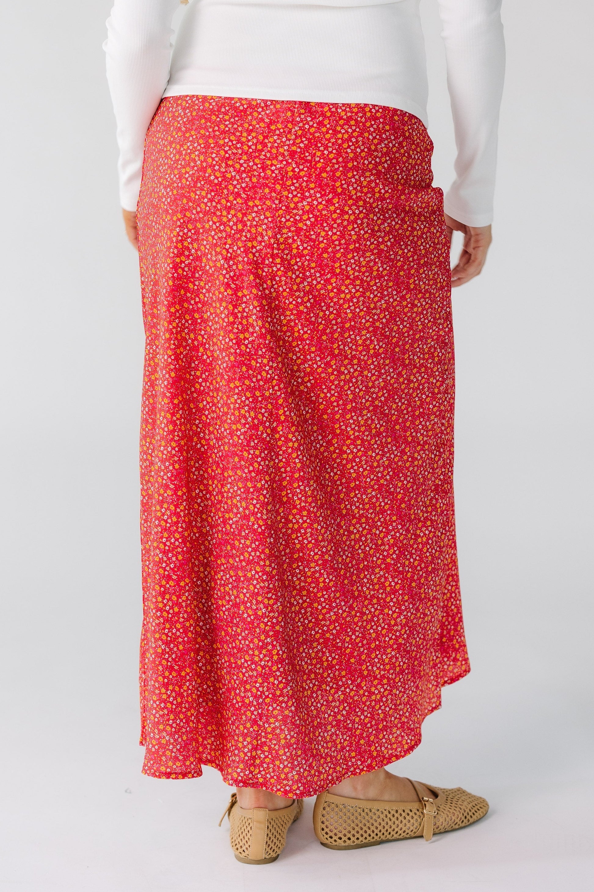 Back view of a woman wearing a red floral midi skirt with a high/low hemline.