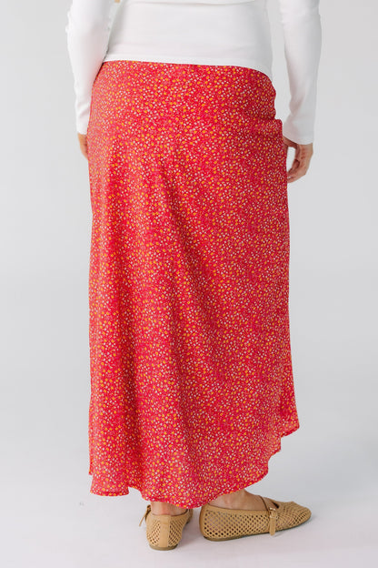 Back view of a woman wearing a red floral midi skirt with a high/low hemline.