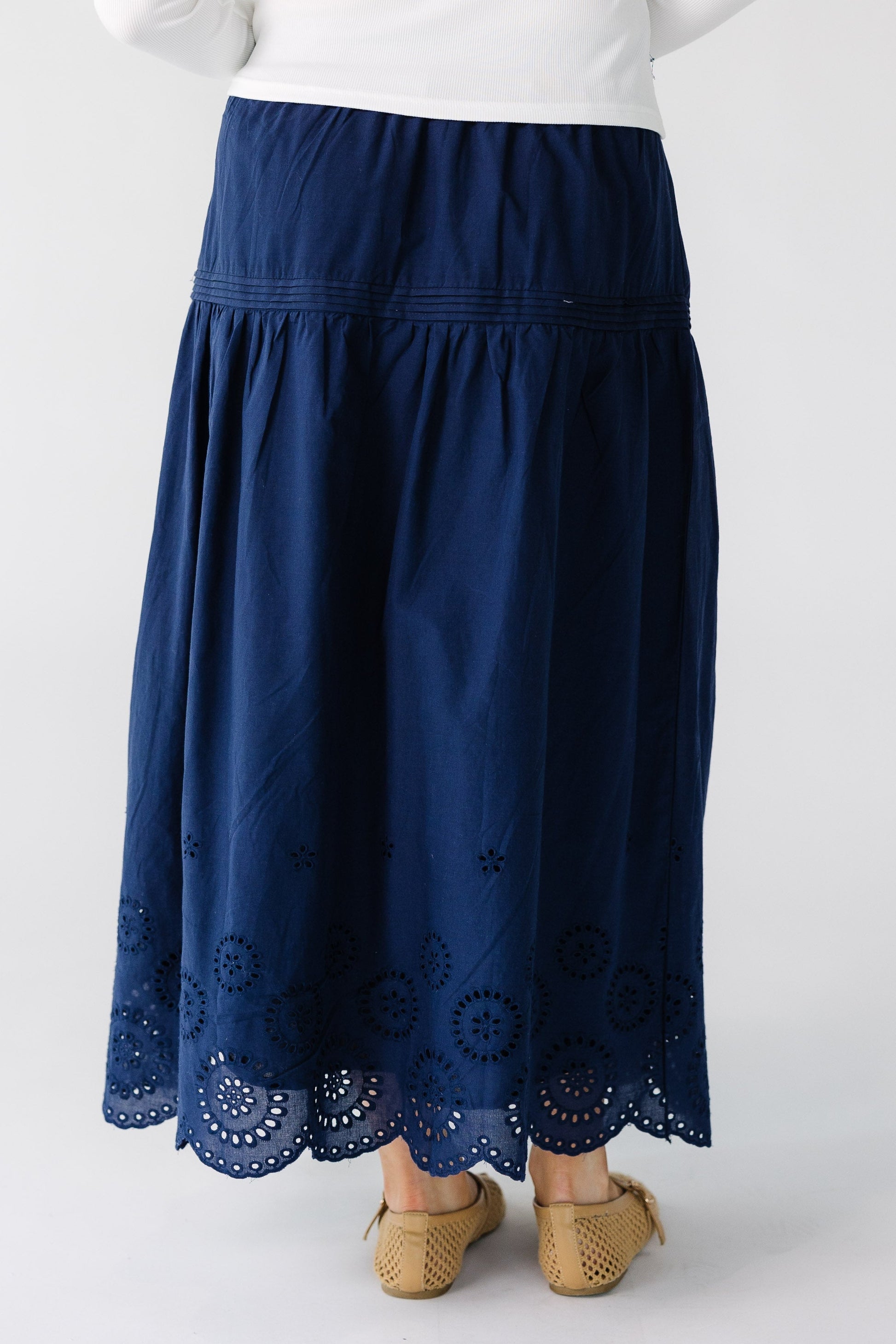 Back view of a woman wearing a navy skirt with an eyelet border pattern.