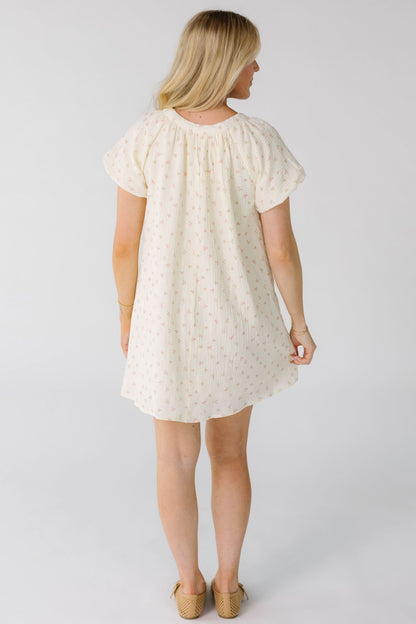 Back view of a woman wearing a cream with pink print mini dress with short balloon sleeves.